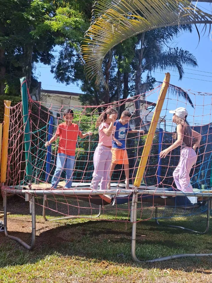 Crianças pulando na cama elástica cercada por rede de proteção