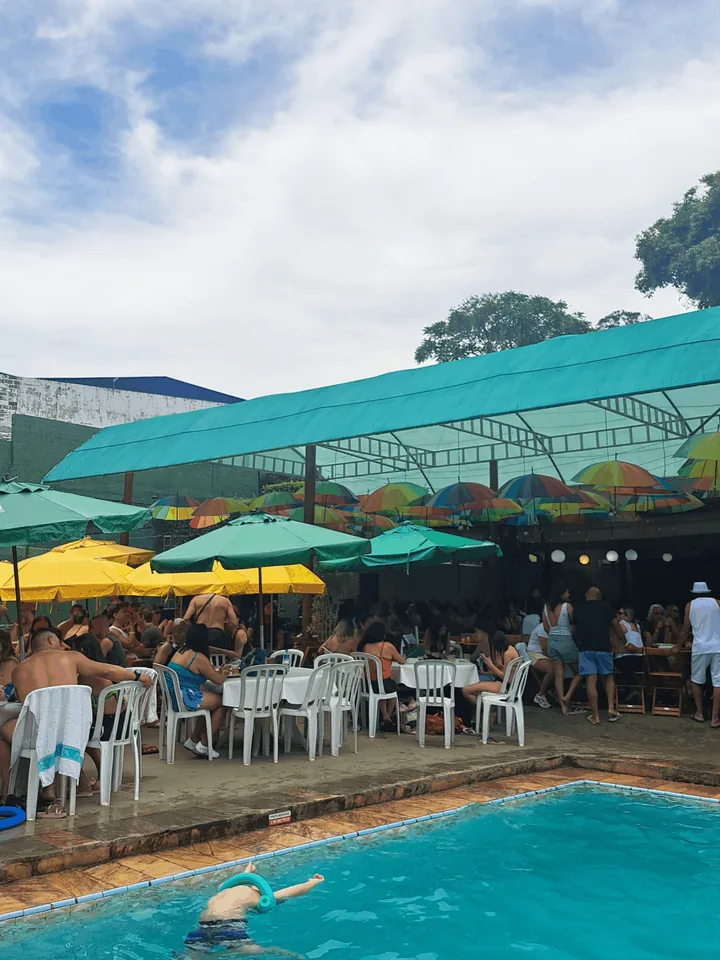 Piscina com nadador e a área de mesas coberta logo atrás