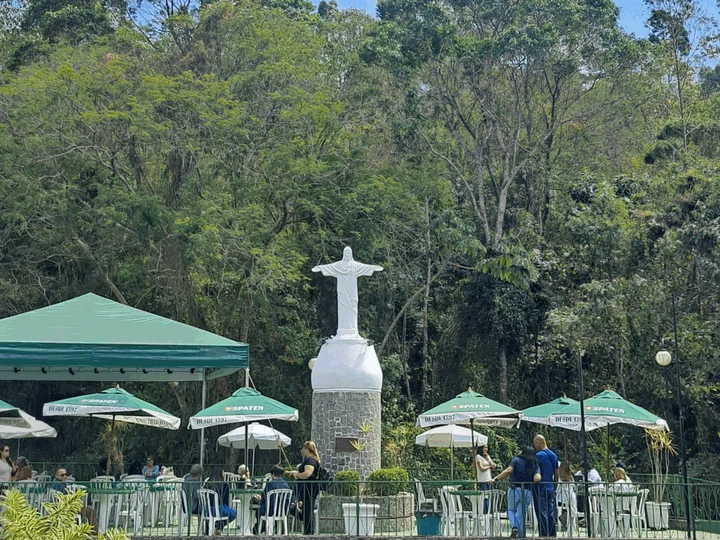 Área de mesas com guarda-sóis verdes e a estátua do Cristo ao fundo