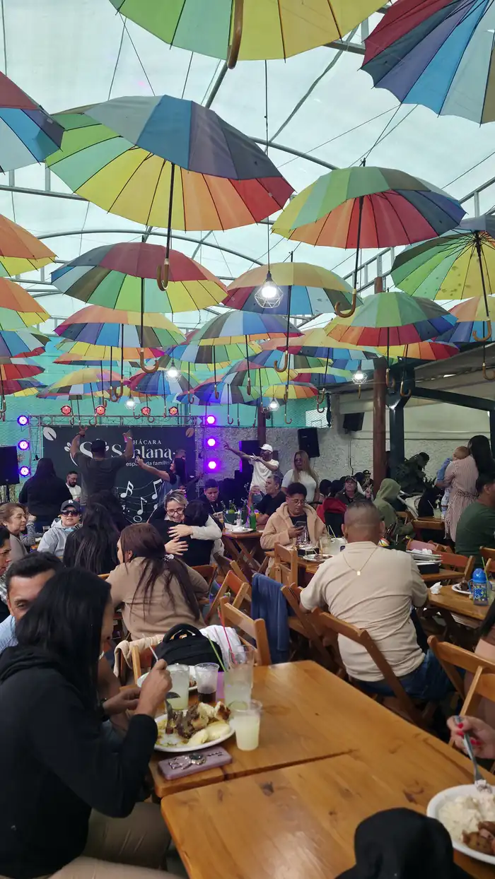 Salão da Chácara Santana em dia de evento: teto de guarda-sóis coloridos, banda no palco e mesas cheias de convidados