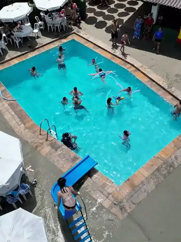 Vista de cima da piscina da Chácara Santana em um domingo de sol, com guarda-sóis coloridos e área de mesas